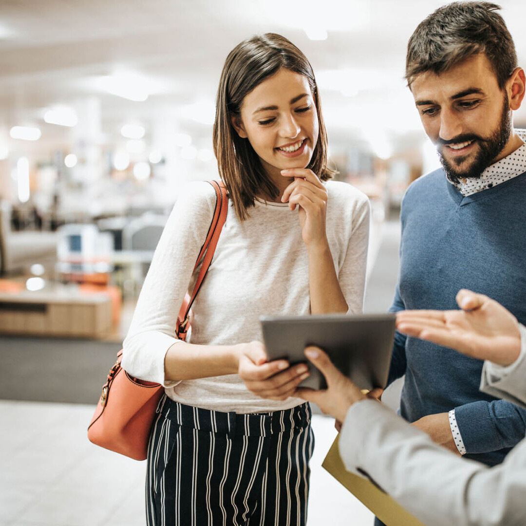 Happy couple and saleswoman using touchpad in furniture store.