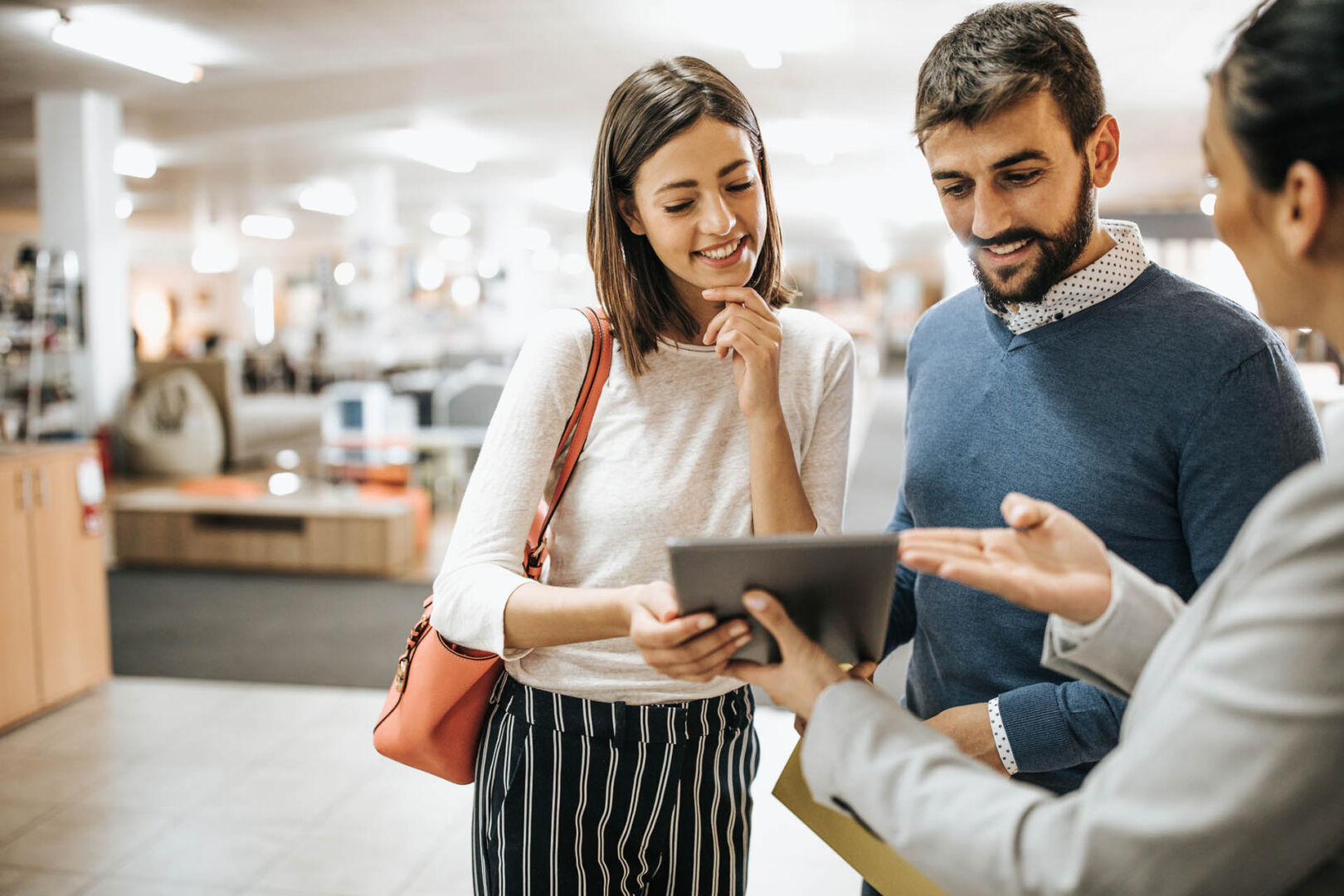 Happy couple and saleswoman using touchpad in furniture store.