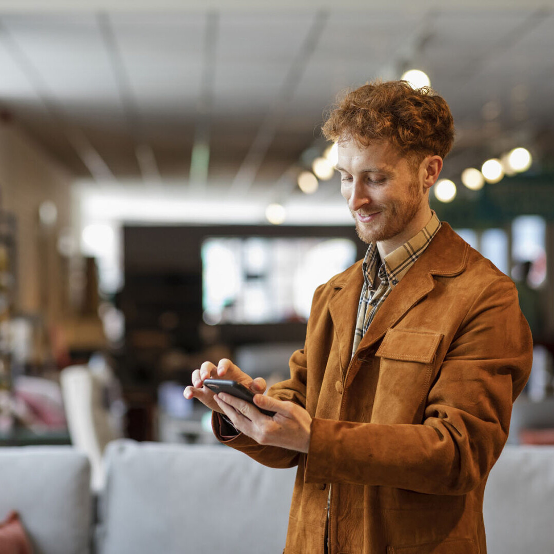 A selective focus of a man with red hair stood looking at his phone as he shops in a furniture department store in Newcastle upon Tyne in the North East of England.