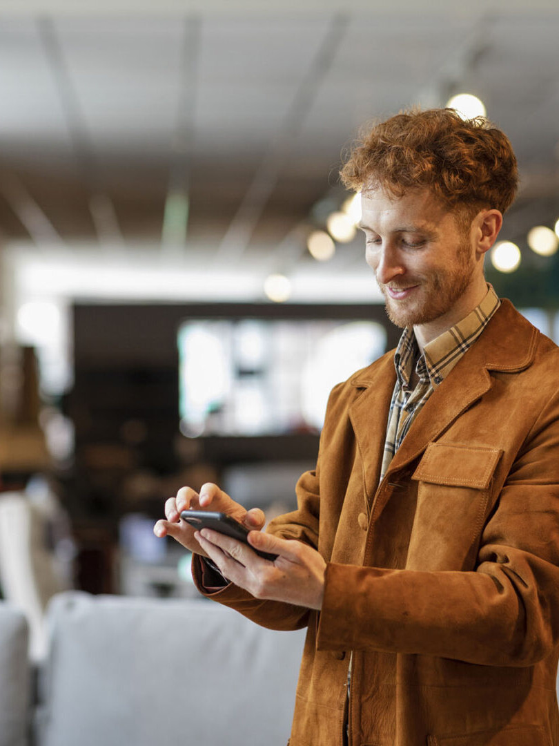A selective focus of a man with red hair stood looking at his phone as he shops in a furniture department store in Newcastle upon Tyne in the North East of England.