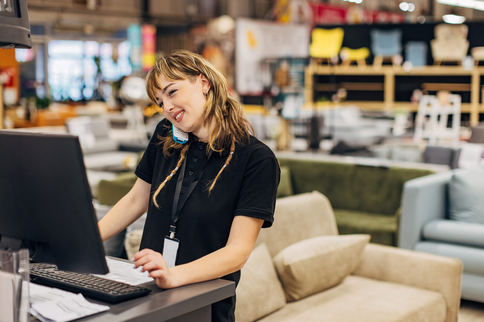 A smiling saleswoman works on a computer in a department store, answers a landline and talks to a customer