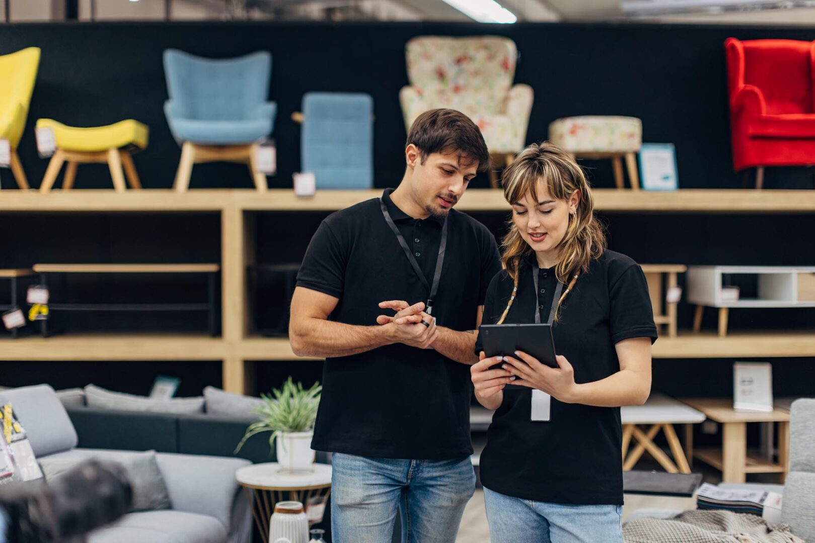 Two salespeople in matching outfits use a digital tablet while working in a furniture store. Teamwork